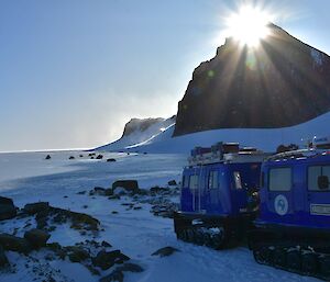 The sun is rising over a mountain peak in the distance with a blue vehicle in the foreground