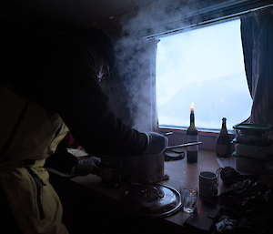 A man is cooking a meal in front of a candle and window