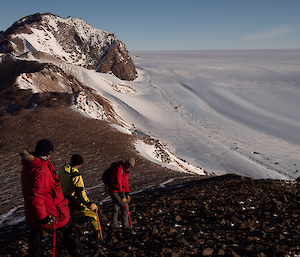 Three men stand atop a mountain crest rising above the snow and ice