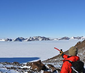 A man is pointing with an ice axe towards mountains in the distance