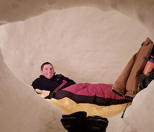A man is relaxing in a sleeping bag inside a snow igloo