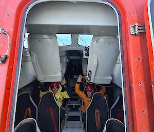 Two smiling people sitting in a red lifeboat that is perched on an angle.