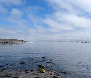 A person in yellow clothing lies on a rocky landscape on the shores of the ocean.