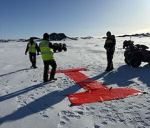 People are placing a big red letter "I" in the snow with plastic panel markers