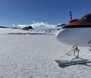 The nose of a red and white plane. The plane is parked on sea ice and the red domes of the field huts can be seen in the background.