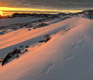 A beautiful sunset in yellow and orange with some artful footprints in the snow in the foreground