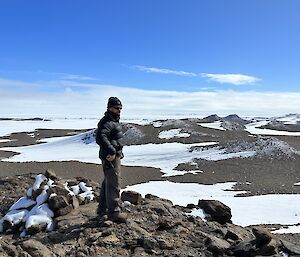 A person in field gear standing on a peak looking across the view