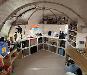 The cozy insides of a completed field hut with a compact kitchen and neat shelving