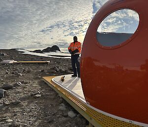 With the edge of a domed red hut in the foreground, a tradie in high-vis enjoys the view