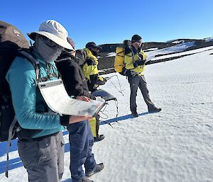 Four people dressed for a cold day out hiking consult their maps