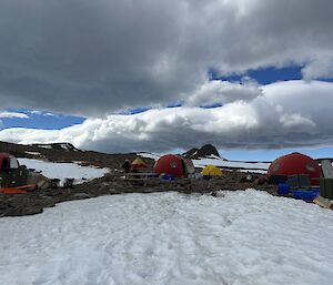 A collection of red domed field huts sit amongst snow and rock