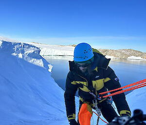 A person in a climbing helmet abseils down a snowy ravine