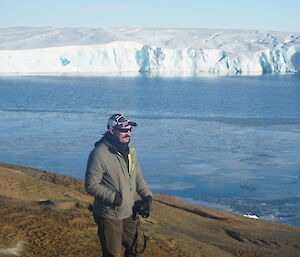 A handsome gent in the foreground on rocks with 100m high ice cliffs in the background across some open water