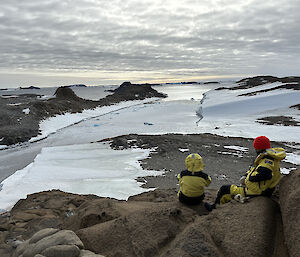Two people in AAD yellow jackets looking out over snow and ice covered islands