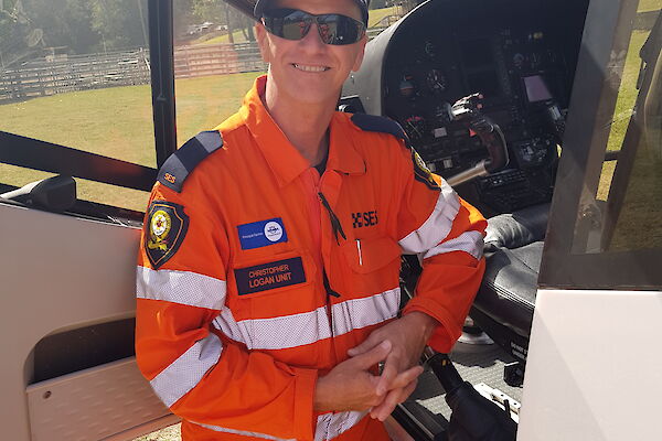 A smiling man in an SES uniform stands by the open pilot's door of a helicopter