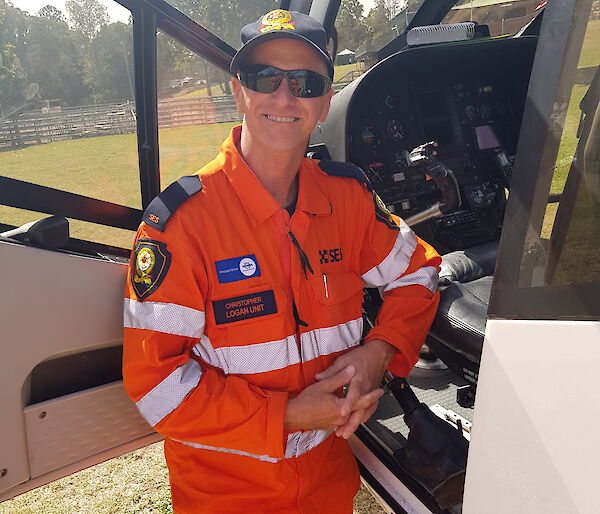A smiling man in an SES uniform stands by the open pilot's door of a helicopter