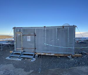 A silver metal hut is tied down to a rocky landscape