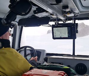 A man driving a vehicle with a rocky, ice covered, range visible through the windshield