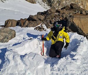 A woman kneels in a hole dug into the snow