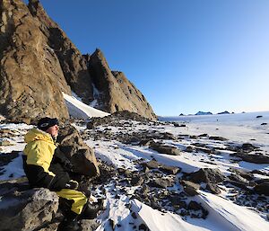 A man looks into the distance while sitting in a rocky, icy, landscape