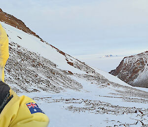 A man is looking into the camera with a steep, rocky and snow covered landscape behind him