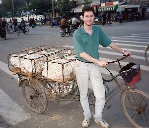 A man is holding a bike that has a cage of geese on the back