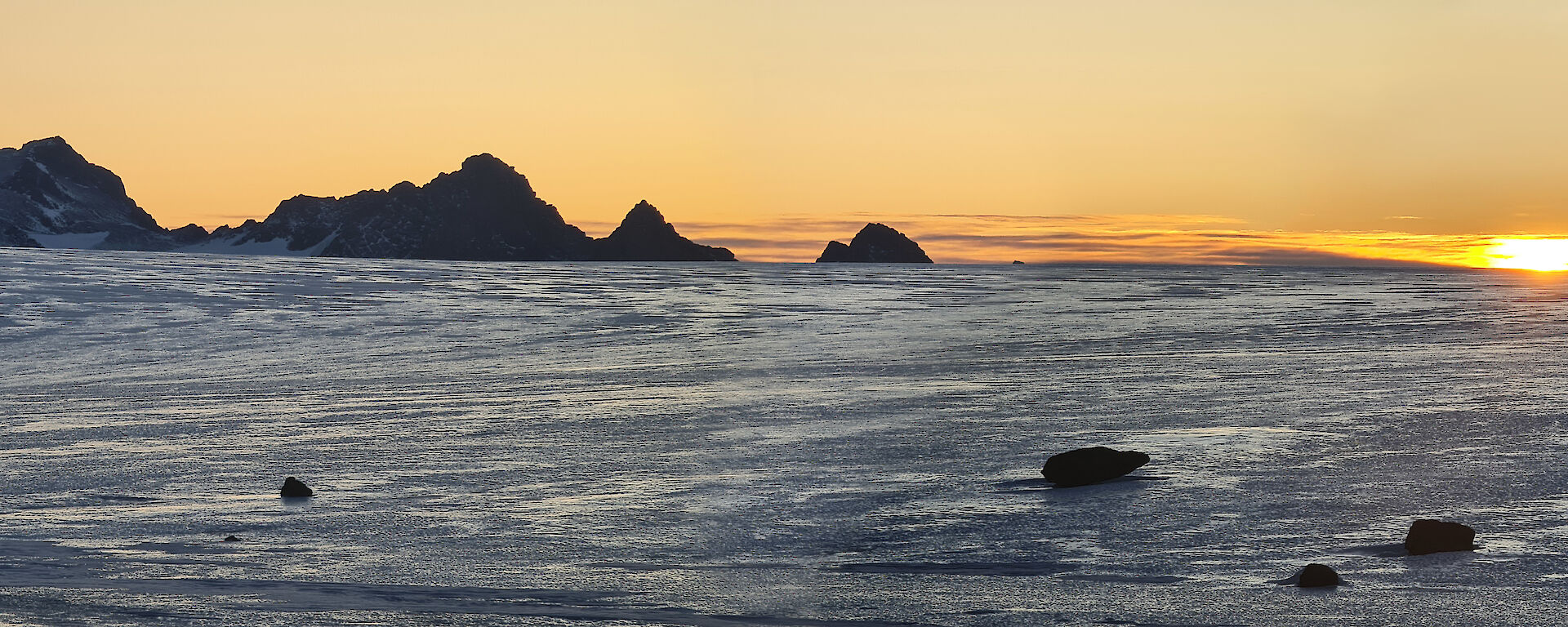 The sun is setting across the ice plateau with a mountain range in the distance