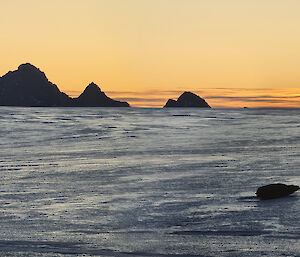 The sun is setting across the ice plateau with a mountain range in the distance