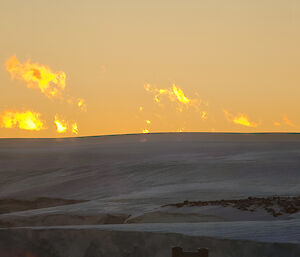 The light from the sun glows behind an ice plain