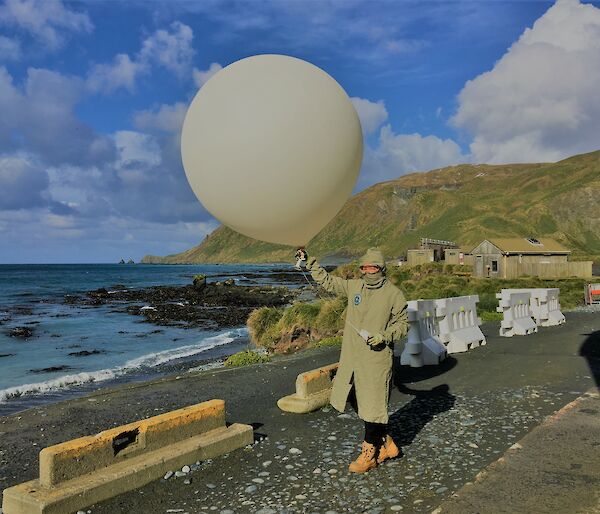A person in brown protective clothing launching a balloon at Macquarie Island