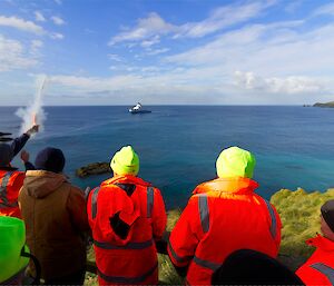 A group of people light a flare as a send-off for a ship in the bay below