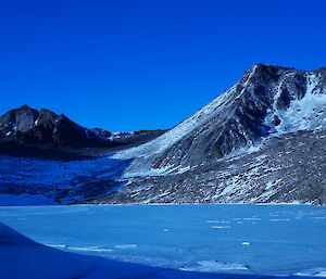 A frozen lake is overlooked by rocky peaks