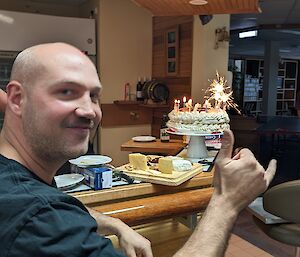 Four people are celebrating a birthday with a cake and cheese platter