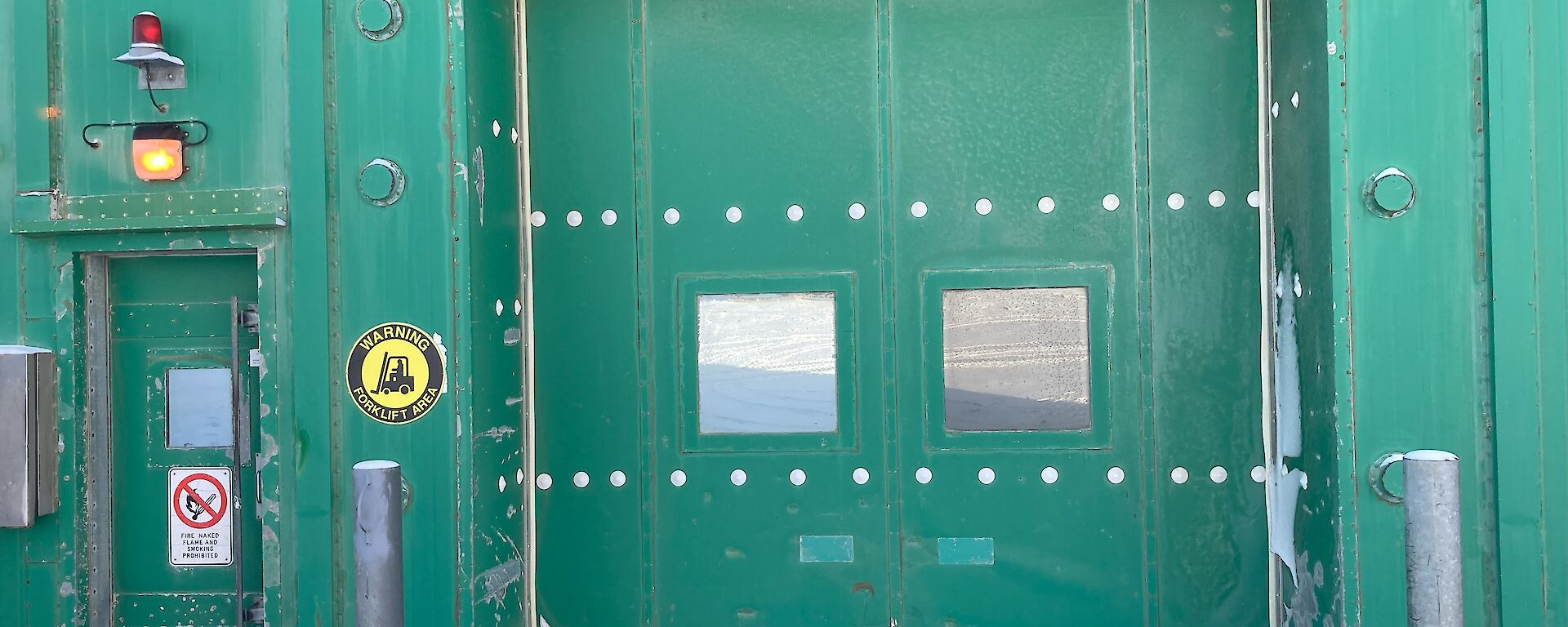 A large green door with two windows on a large green industrial shed