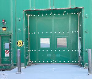 A large green door with two windows on a large green industrial shed