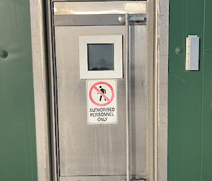 A silver metal door set into a green building. The door has a sign on it that says, "Authorised Personnel Only".