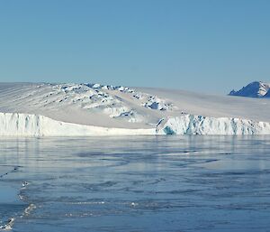 A rocky mountain range is in the far distance beyond ice cliffs and sea