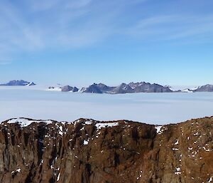 Two rocky peaks bracket a rocky mountain range in the distance across an ice plateau