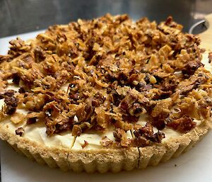 This photo frame is filled with a cheesecake, topped with crispy corn flakes and nuts, sitting on a white plastic serving platter.