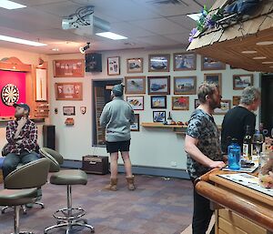 People are gathered in a bar area with a dart board in the background