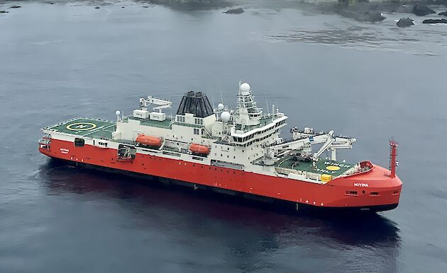 A large ice breaking ship sits in the calm waters with mountainous Macquarie Island behind
