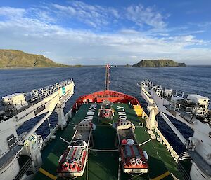 The bow of a ship pointed towards Macquarie Island with amphibious vehicles on board
