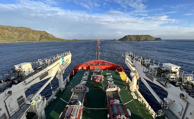 The bow of a ship pointed towards Macquarie Island with amphibious vehicles on board