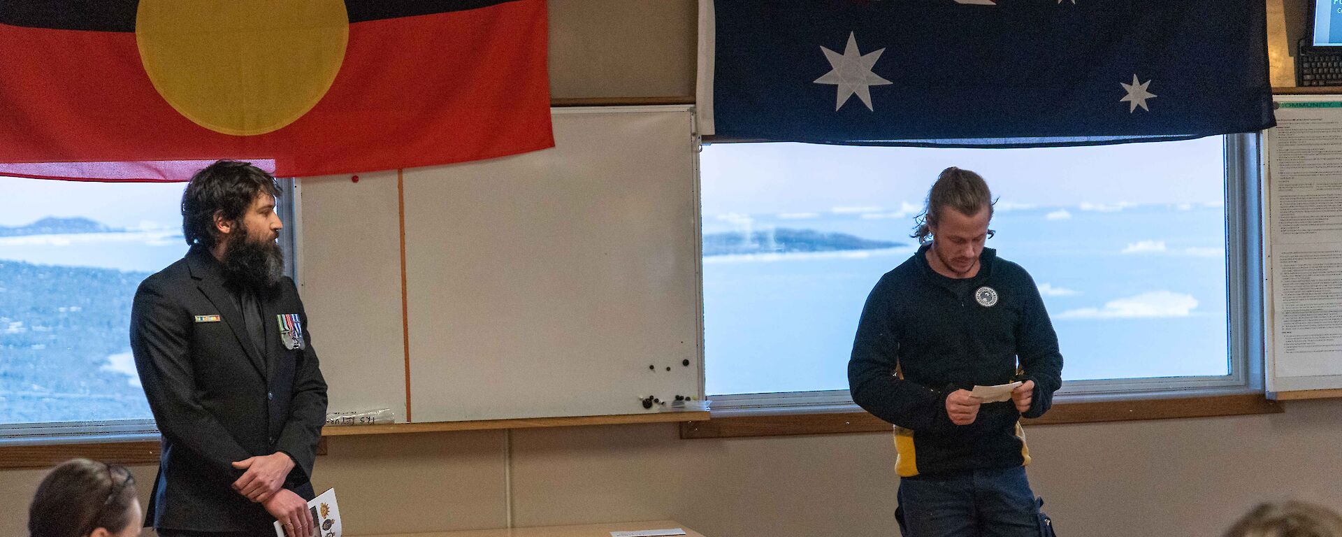 Two men stand in front of the Australian and Aboriginal flags during an Anzac Day service at Davis station