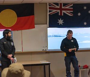 Two men stand in front of the Australian and Aboriginal flags during an Anzac Day service at Davis station