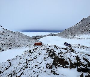 A red hut is surrounded by snow and ice covered rocky terrain