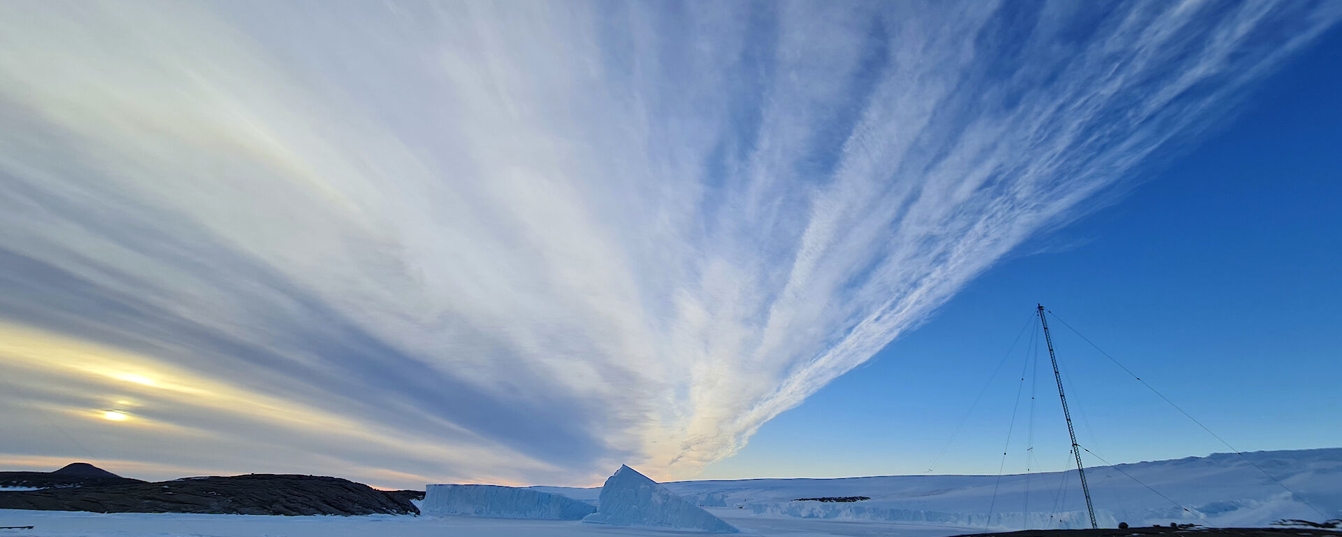 Strings of clouds in a blue sky stretch into the distance over icebergs