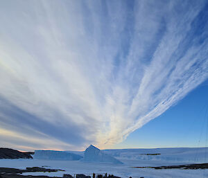 Strings of clouds in a blue sky stretch into the distance over icebergs