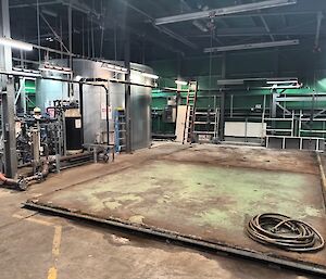 This photo is largely comprised of a bare concrete floor, where the water tank stood for many years. The left and the rear of the photo are the walls of the shed covered in framework and pipes. In the back left of the photo stands the new steel cylindrical water tank.