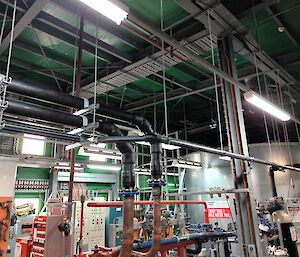 This photo is an overview of the Tank House with pipes of various sizes suspended from the roof and stretching across the floor. In the right rear of the photo is the large new steel cylindrical water tank.